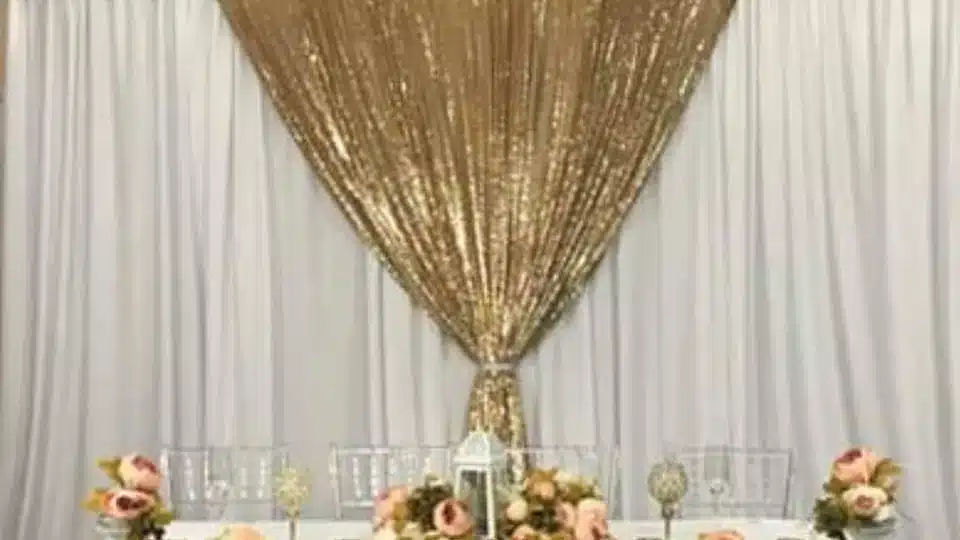 White backdrop drapes with a gold sequin center panel behind a table with pink roses