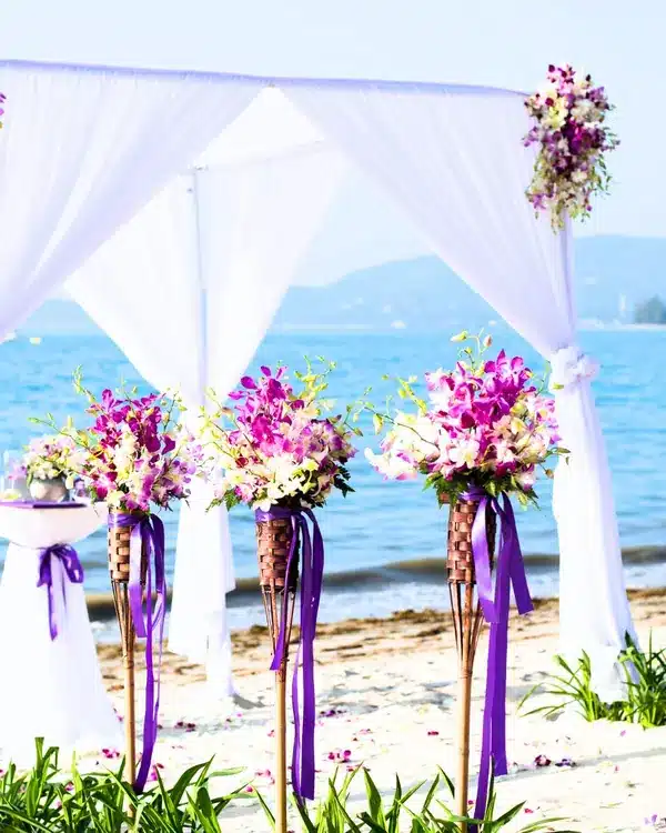 White draped canopy with purple ribbons and orchids set up for a ceremony on a beach