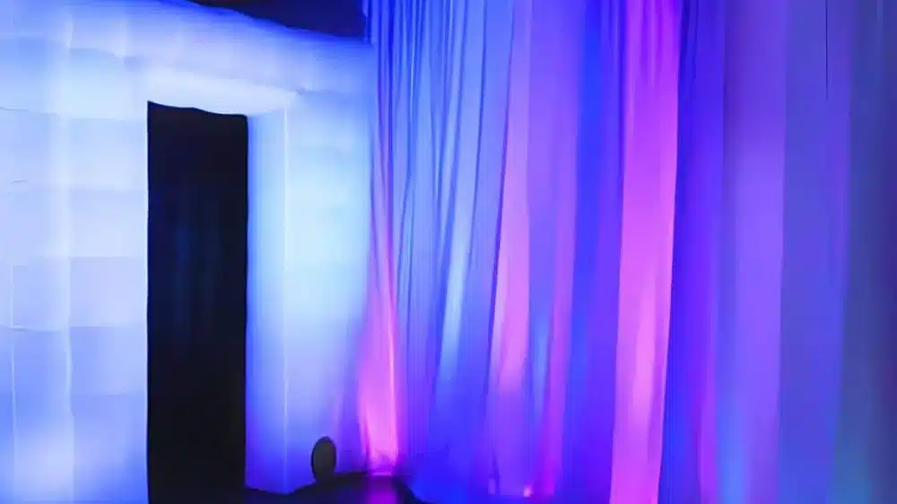 Glowing white inflatable photo booth beside drapes washed in blue and pink light