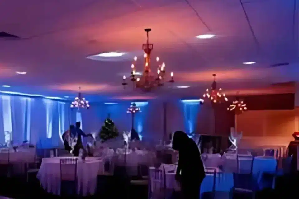 Reception hall lit with blue and warm uplighting colors, with chandeliers over the tables