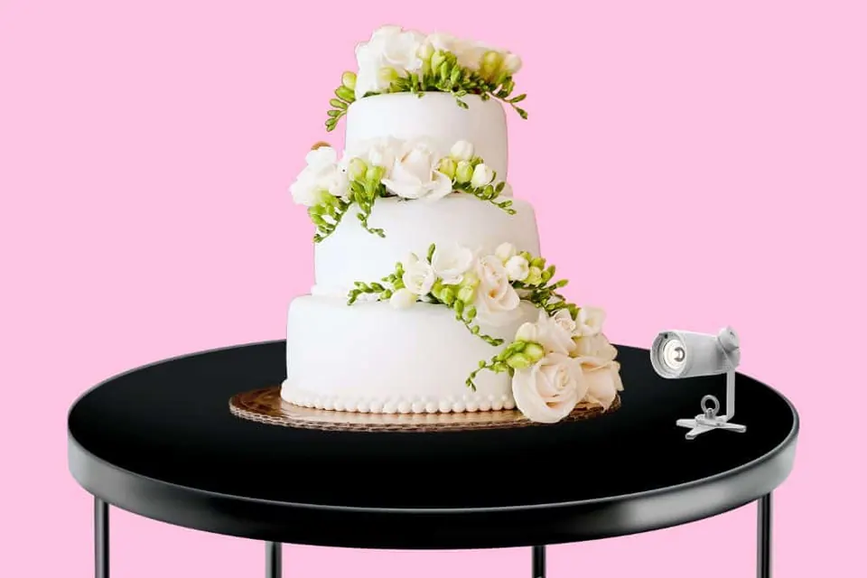 Three-tier white wedding cake on a black table with a small pin spot light beside it