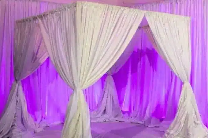 White fabric canopy booth with draped corners in front of drapes lit purple