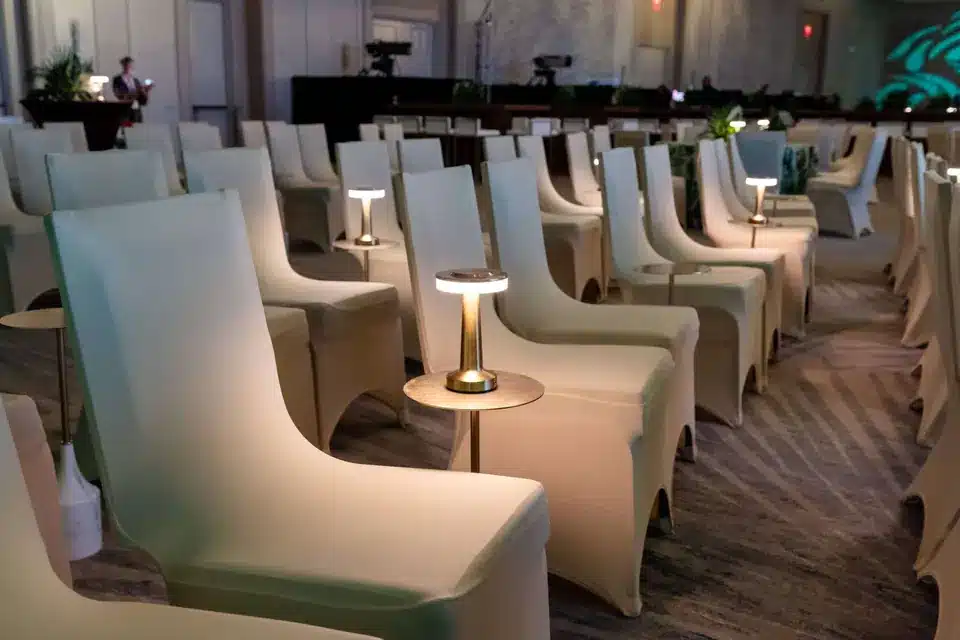 Rows of chairs dressed in white stretch chair covers with small lamps between them