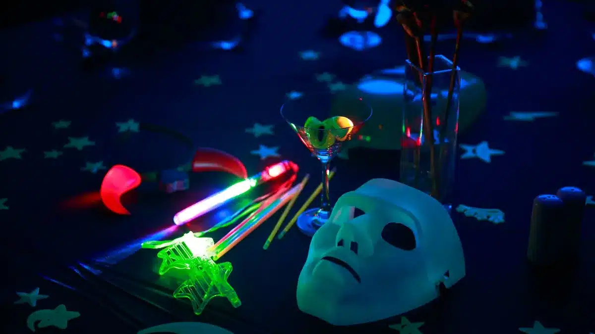 Glow sticks, a glowing star wand, red glowing horns and a white mask on a dark party table