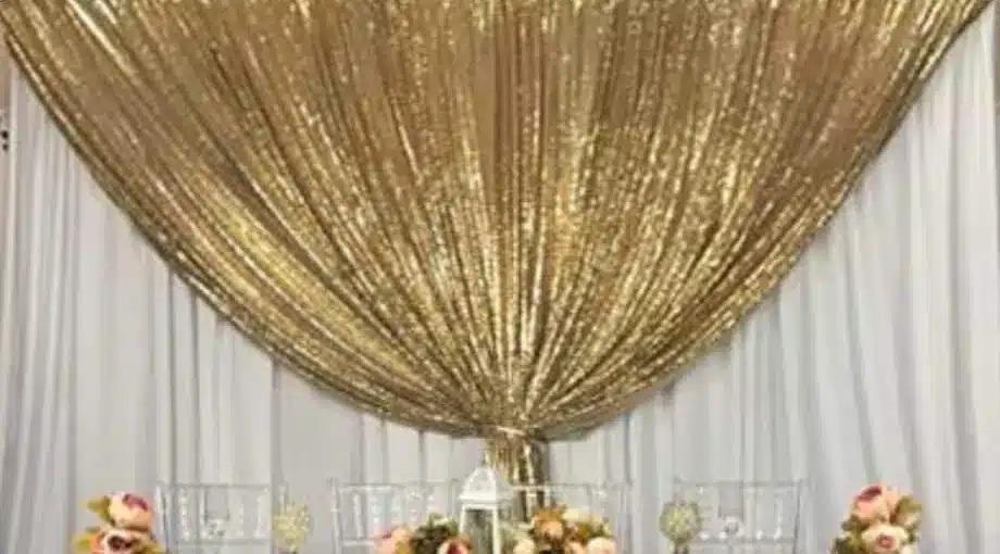 Gold sequin swag draped in a wide curve over white backdrop drapes above a head table with pink flowers