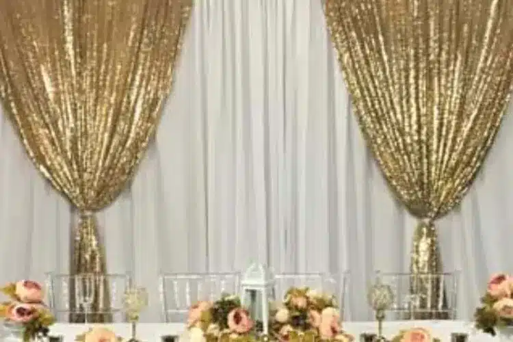 Gold sequin and white drape wall behind a table with white and pink flowers