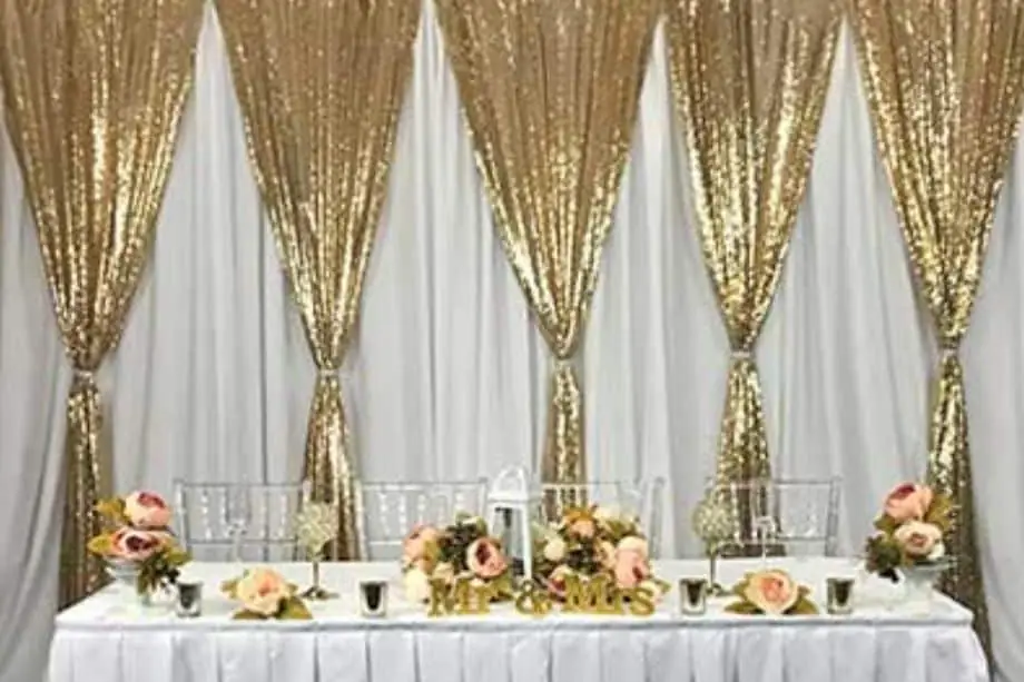 Head table in front of white drapes with gold sequin panels and pink rose arrangements