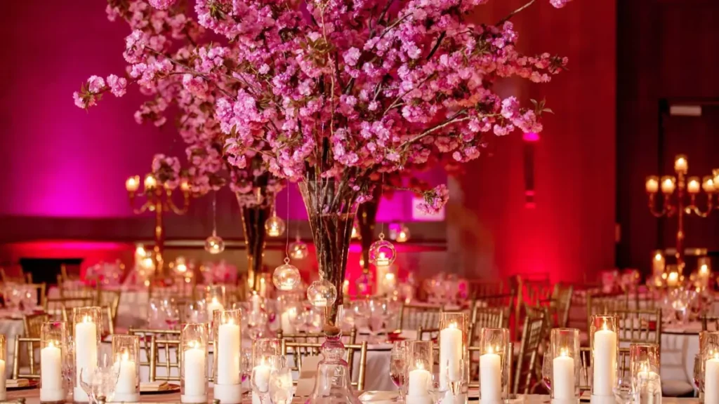 Reception tables with candles and tall pink blossom centerpieces under pink uplighting