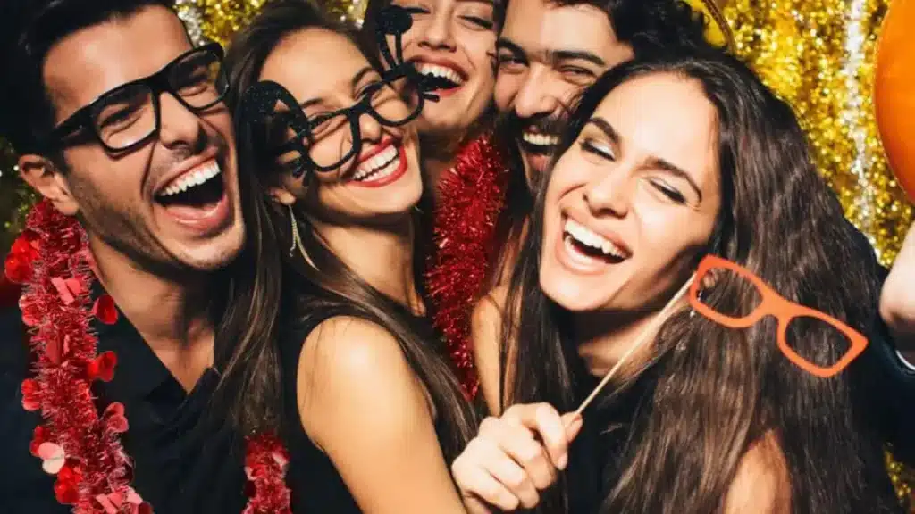 Friends laughing and posing with eyeglasses photo booth props in front of a gold tinsel backdrop