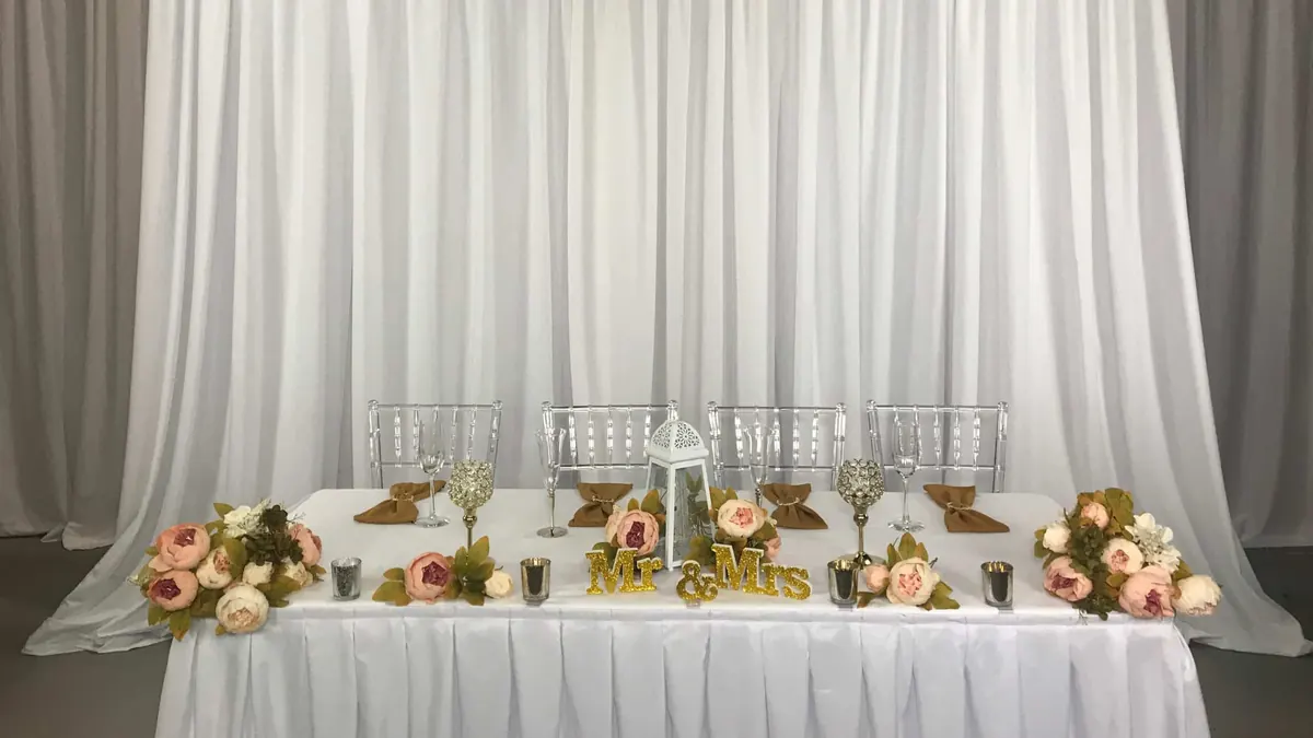 White pipe and drape backdrop behind a head table set with peach roses and candles