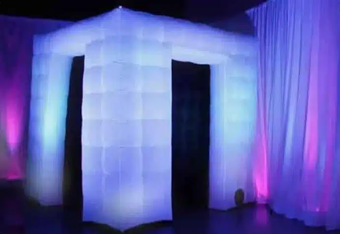 White inflatable photo booth lit from inside, beside drapes in purple light