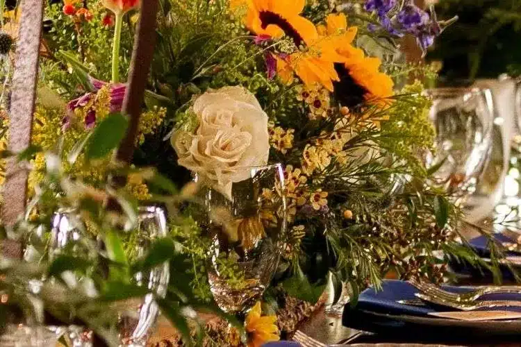 Sunflower and white rose centerpiece with greenery beside navy napkins and glassware