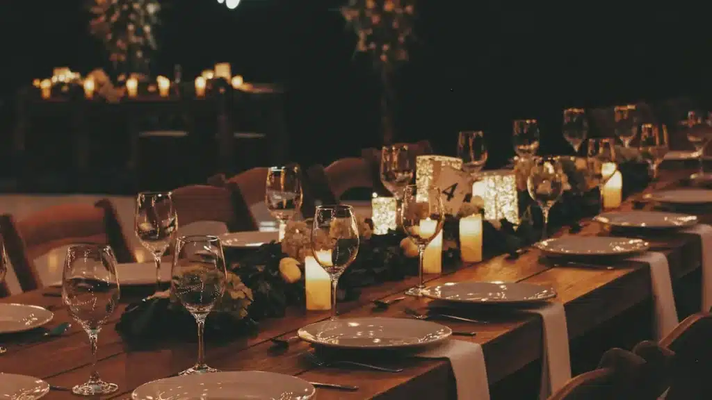 Long candlelit reception table set with plates, glasses and greenery at an evening wedding