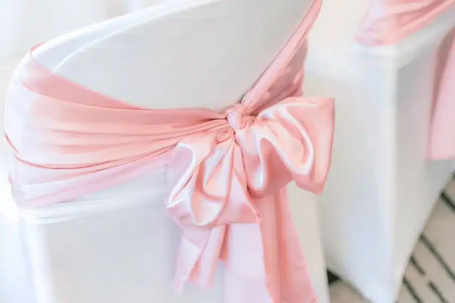 Pink satin sash tied in a bow on a white spandex chair cover