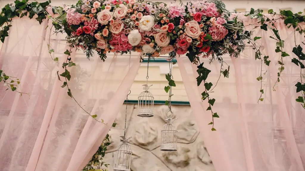 Backdrop of blush sheer drapes under a garland of pink roses and ivy, with white birdcage lanterns hanging in the center