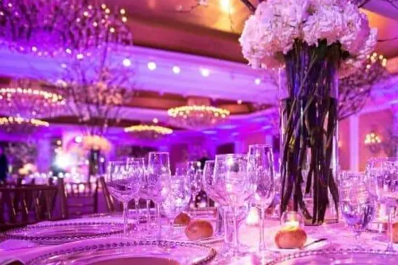 Reception tables with tall white floral centerpieces under pink and purple uplighting