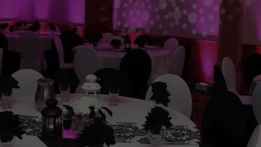 Round tables with white and black chair covers in a room lit pink and purple, with a dot light pattern on the wall