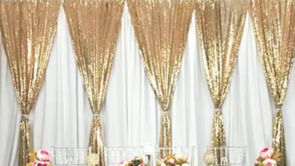 White drapes with tied-back gold sequin panels behind a long head table with pink flowers