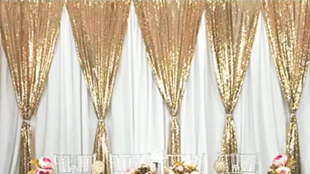 White drapes with tied-back gold sequin panels behind a long head table with pink flowers