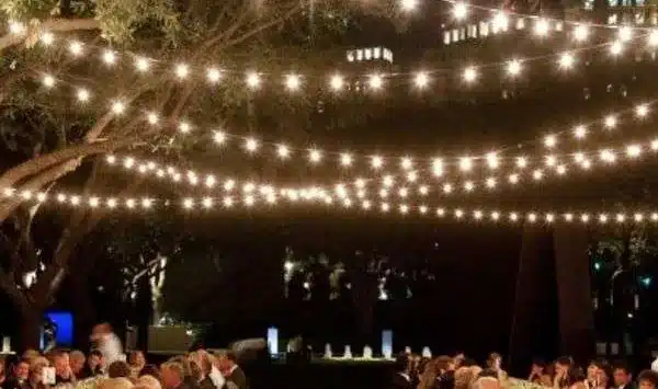 Strings of warm bistro lights hanging over long dinner tables set on a lawn at night