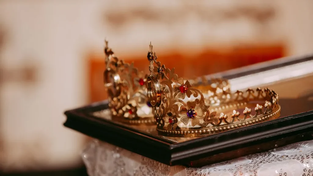 Two jeweled gold crowns on a tray over a lace-covered table