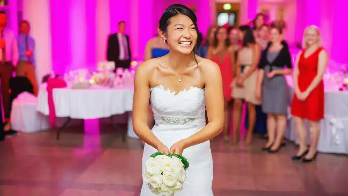 Smiling bride holding a white bouquet in a reception hall washed in pink uplighting