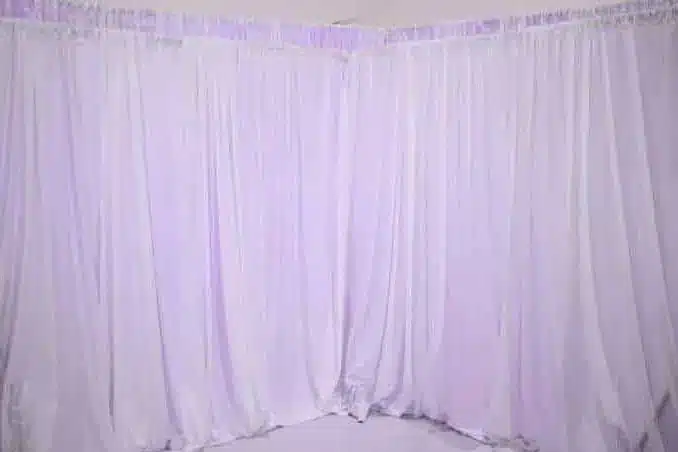 White drapes on a backdrop frame set up around the corner of a room in soft purple light