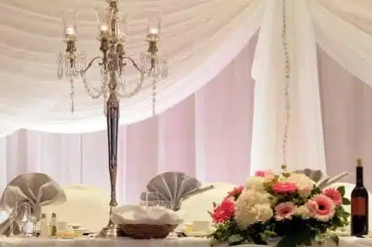 Head table with white draped fabric, white chair covers, a crystal candelabra and pink flowers