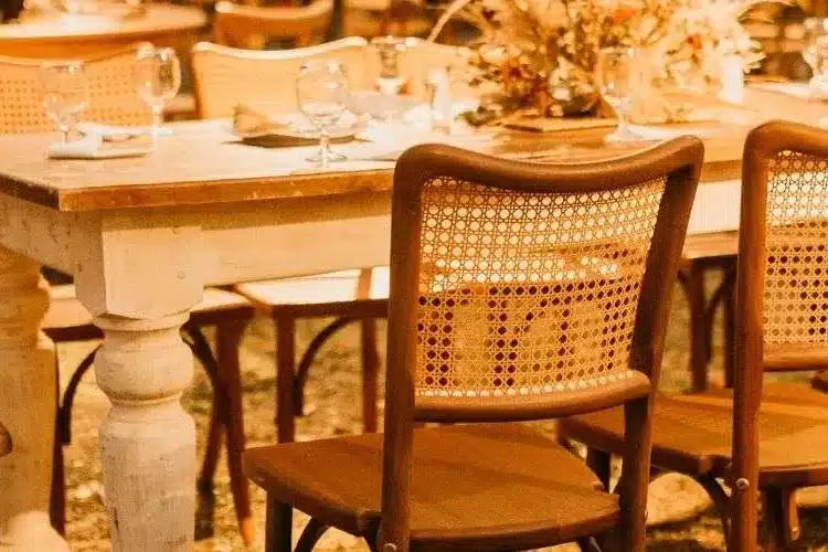 Wooden dining table with rattan-back chairs and glassware under warm light